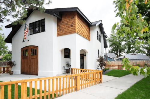 A modern two-story house with a wooden garage door, white exterior, and a wooden fence in front.